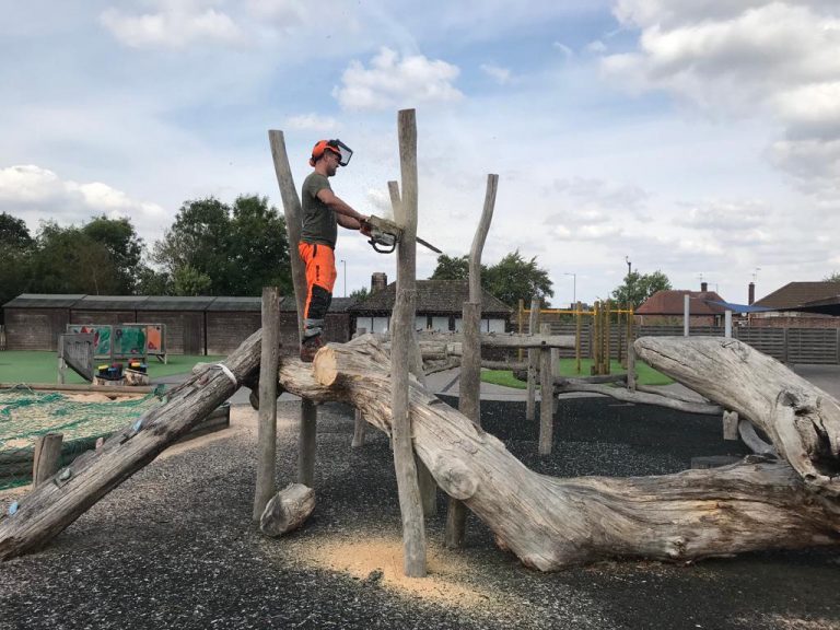 Climber sectioning a large log using a chainsaw on a playground job