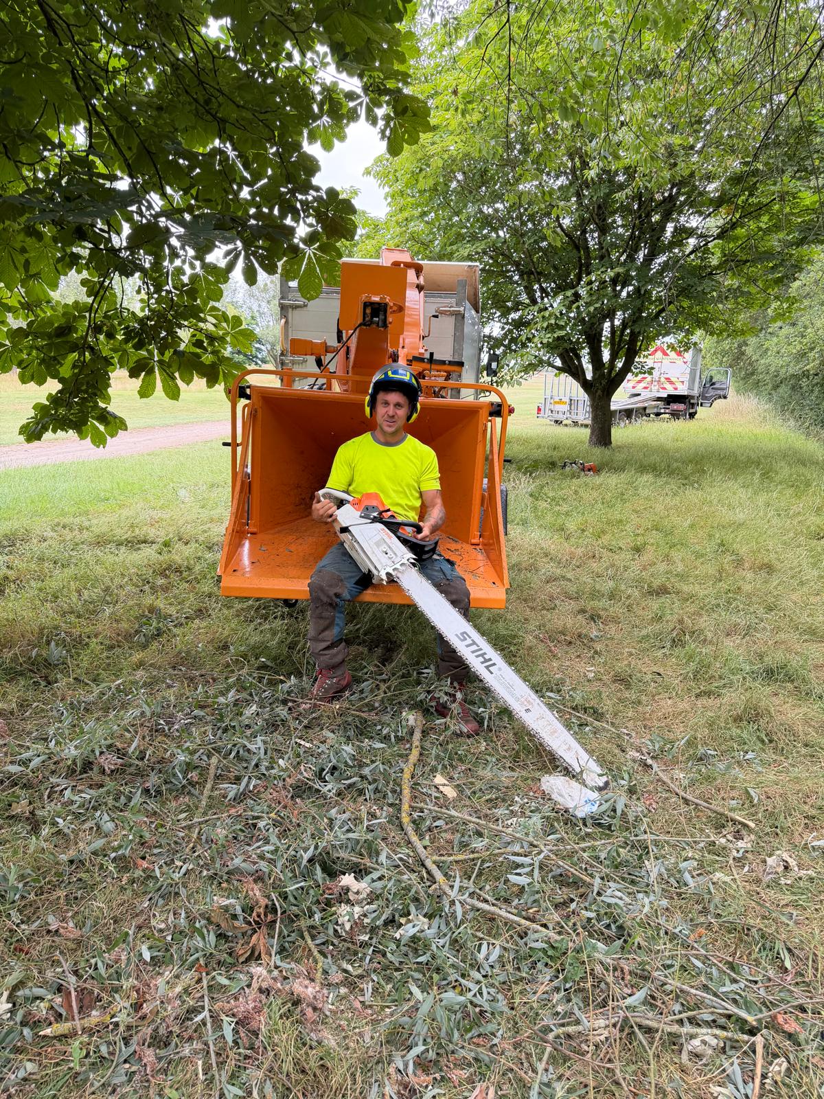 NPTC-qualified arborist with a professional chainsaw beside a woodchipper